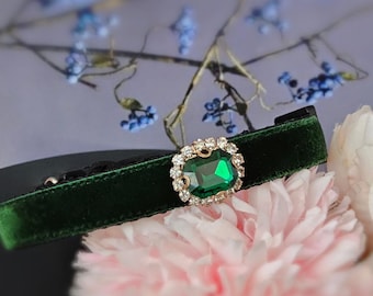 May include: A dark green velvet choker with a gold-toned clasp and a large, square-shaped emerald green rhinestone surrounded by smaller clear rhinestones.