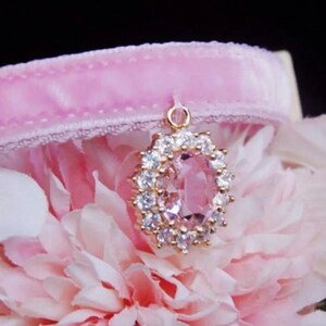May include: A pink velvet choker with a gold pendant featuring a large oval-shaped pink gemstone surrounded by smaller clear gemstones.