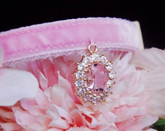 May include: A pink velvet cat collar with a gold pendant featuring a large pink crystal surrounded by smaller clear crystals.