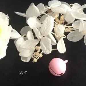 May include: A pink bell charm with white dried flowers and a white rose.