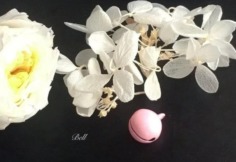 May include: A pink bell charm with white dried flowers and a white rose.