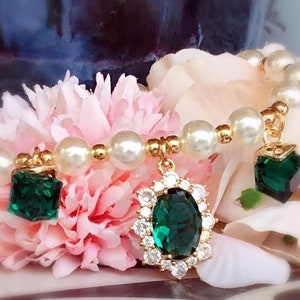 May include: A gold bracelet with white pearl beads and three green gemstone charms. The charms are a square, a round, and an oval shape.