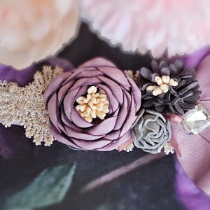 May include: A delicate white lace collar with a purple flower embellishment. The flower is made of fabric and has a layered design. The collar is adorned with small, sparkly accents.