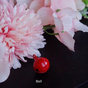 May include: A red bell with a pink flower arrangement in the background. The bell is on a black surface. The text "Bell" is below the bell.