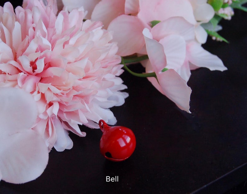 May include: A red bell with a pink flower arrangement in the background. The bell is on a black surface. The text "Bell" is below the bell.