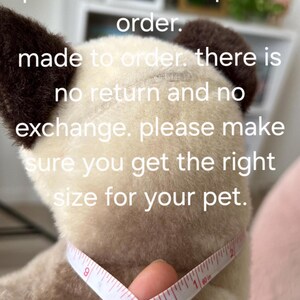 May include: Close-up of a white stuffed animal with brown ears being measured around the neck with a white tape measure. The tape measure reads 9, 10, 1, and 2. The text on the image reads "please measure your pet neck before place order. made to order. there is no return and no exchange. please make sure you get the right size for your pet."