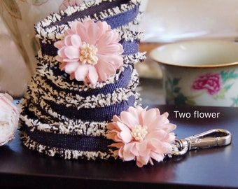May include: A black and white striped fabric with two pink fabric flowers attached. The fabric has a frayed edge. The fabric is attached to a silver key chain.
