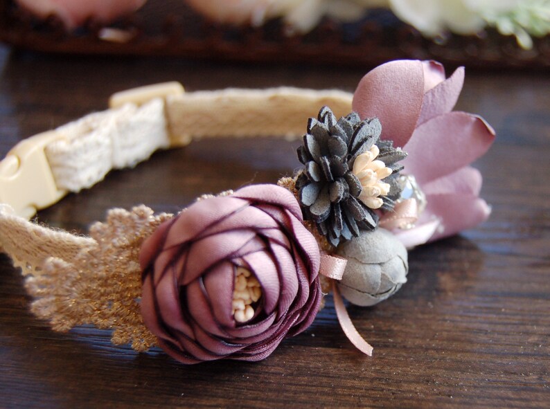 May include: A delicate, handmade pet collar with a burlap base and lace trim. It features a cluster of purple, gray, and white fabric flowers.