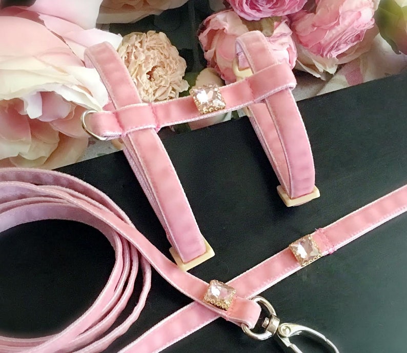 May include: Pink velvet dog harness and leash set with crystal accents. The harness has a D-ring for attaching a leash. The leash has a clip for attaching to the harness.