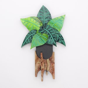 May include: A wooden plant-shaped wall hanging. The leaves are green and lime green with dark green veins. The pot is black, and the stand is brown with white glitter accents. The wall hanging is a decorative item.