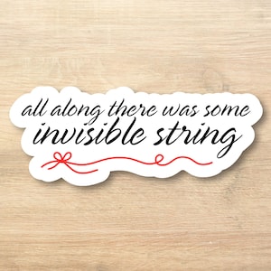 May include: White sticker with the text "all along there was some invisible string" in black script. A red bow and line accent the bottom of the text. The sticker is on a light wood grain surface.