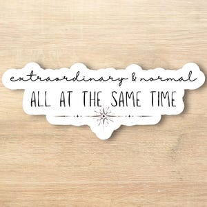May include: A white sticker with the words "extraordinary & normal ALL AT THE SAME TIME" in black script and block letters. A small starburst design is below the text, and the sticker has a white border.