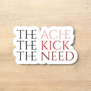 Può includere: Un adesivo bianco con le parole "THE ACHE, THE KICK, THE NEED" in nero e sfumatura rossa. L'adesivo è su una superficie di legno chiaro.