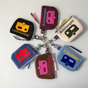 Könnte beinhalten: Sechs bunte Stoff-Münzbeutel mit einem Wohnmobil-Design und dem Text "Brötchen­geld" auf jedem. Die Beutel sind an einem silbernen Schlüsselanhänger befestigt.