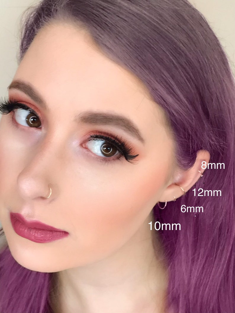 Young teenaged girl with purple hair and infinity hoop ring piercings in nose and ear, sizes identified with text showing best options for lobe, conch and helix.