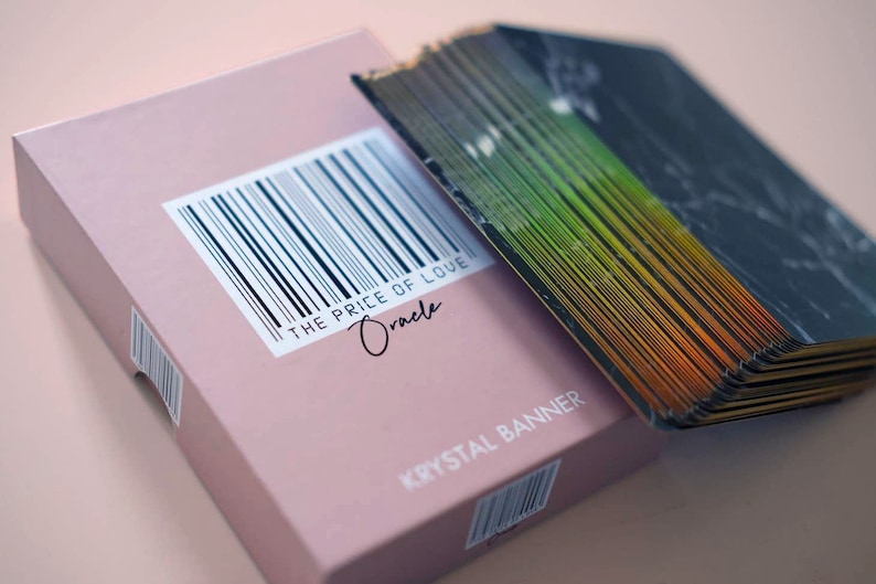 Puede incluir: Una caja rosa con un c&oacute;digo de barras y el texto "THE PRICE OF LOVE Oracle" y "KRYSAL BANNER". La caja est&aacute; abierta y se ve una baraja de cartas con un dise&ntilde;o negro e iridiscente arco&iacute;ris.