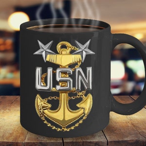 May include: Black coffee mug with a gold anchor, silver stars, and the text "USN" on a black background.