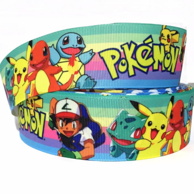 May include: A blue and green ribbon with a rainbow stripe pattern featuring Pokemon characters including Pikachu, Squirtle, Bulbasaur, and Ash Ketchum. The ribbon has the word "Pokemon" printed on it.