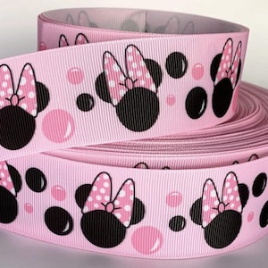May include: A spool of light pink grosgrain ribbon featuring a repeating pattern of black mouse silhouettes with pink and white polka-dot bows, interspersed with various sizes of solid black and light pink circular polka-dot accents.