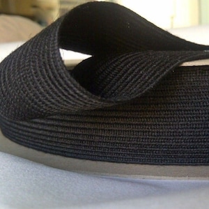 May include: Black elastic trim with a ribbed texture. The trim is rolled up on a cardboard roll.
