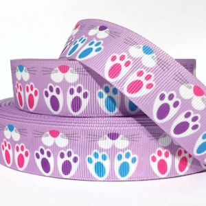 May include: Purple ribbon with a repeating pattern of white bunny paw prints, pink bunny noses, and blue bunny whiskers.