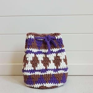 May include: A crocheted drawstring bag with a brown, white, and purple geometric pattern.