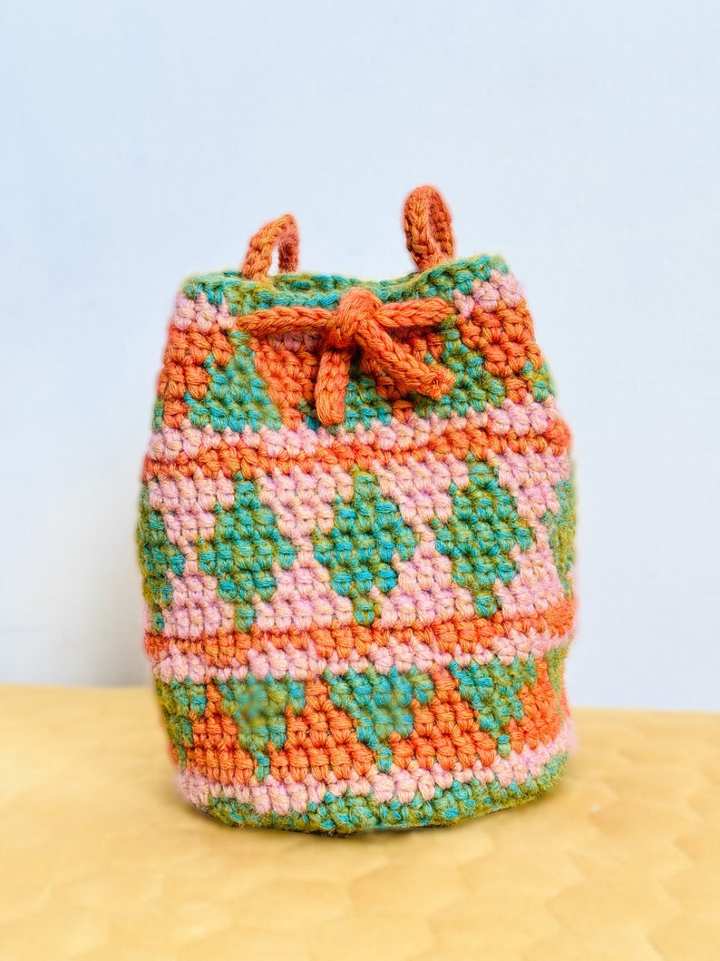 May include: A small, crocheted drawstring bag with a geometric pattern in shades of orange, pink, and green.