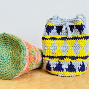 May include: Two crocheted bags, one green and pink, the other grey, yellow, and blue. Both bags have a geometric pattern.
