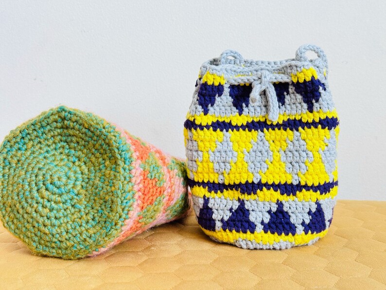 May include: Two crocheted bags, one green and pink, the other grey, yellow, and blue. Both bags have a geometric pattern.