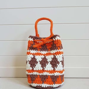 May include: A small crocheted bag with a drawstring closure. The bag is made with brown, white, and orange yarn and has a geometric pattern. The bag has a single handle.