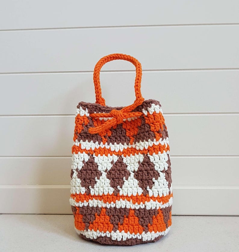 May include: A small crocheted bag with a drawstring closure. The bag is made with brown, white, and orange yarn and has a geometric pattern. The bag has a single handle.