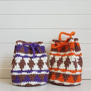 May include: Two crocheted drawstring bags with geometric patterns. One bag is brown, white, and purple. The other bag is brown, white, and orange.