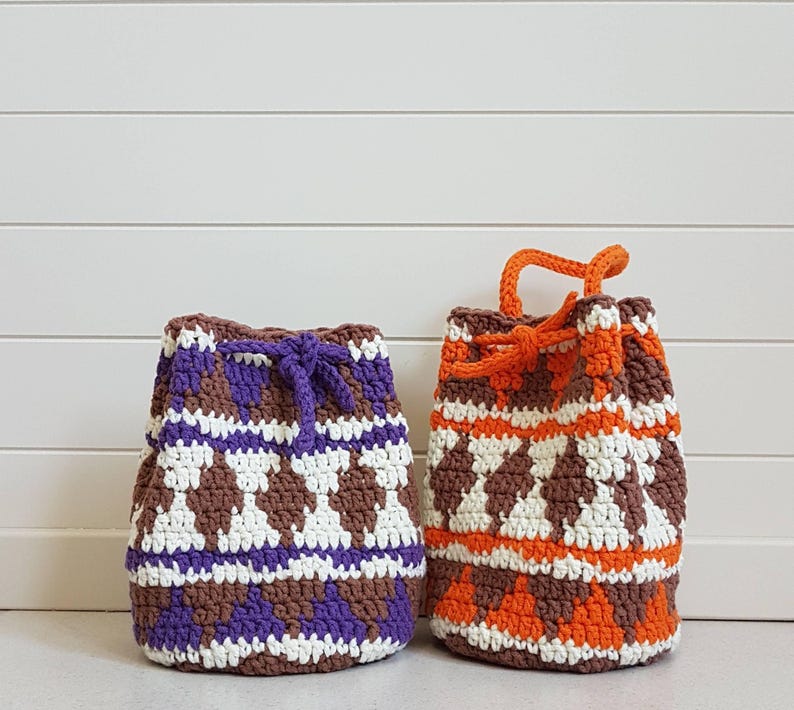 May include: Two crocheted drawstring bags with geometric patterns. One bag is brown, white, and purple. The other bag is brown, white, and orange.