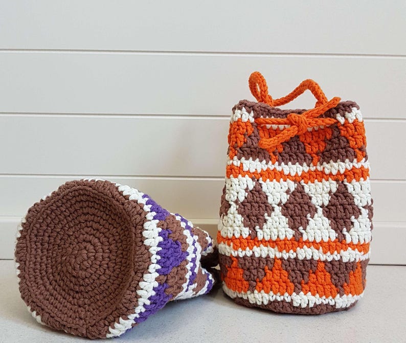 May include: Two crocheted drawstring bags, one brown, white, and orange, and the other brown, white, and purple.