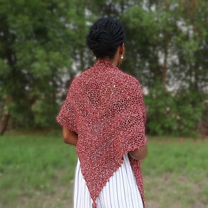 May include: A red and silver crochet shawl with a fringed edge. The shawl is draped over the shoulders of a person with black hair.