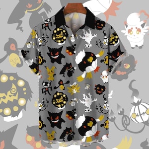May include: Gray button-up shirt with a black collar and short sleeves. The shirt features a repeating pattern of various cartoon monsters in black, yellow, and white. The shirt is hanging on a wooden hanger.