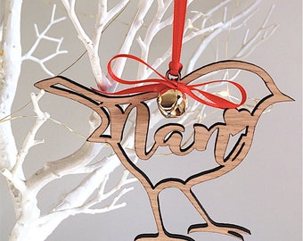 May include: Wooden bird ornament with the word "Nan" cut out. The bird is made of light brown wood with a black outline. It hangs from a red ribbon and a small gold bell. The ornament is displayed against a white background.