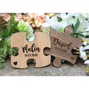 Puede incluir: Dos piezas de rompecabezas de madera con los nombres Malin y David y la fecha 18.07.2016 grabados en ellas. Las piezas están unidas y tienen una forma de corazón recortada.