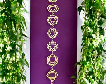 May include: A gold metal chakra wall hanging with seven different chakra symbols, each with a unique design. The hanging is attached to a white tassel.