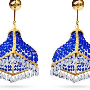 May include: Two matching pendant lights with a gold frame and a blue crystal design. Clear crystal teardrops hang from the bottom. The lights are suspended from a gold ceiling mount.