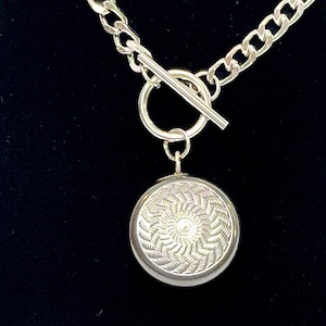 May include: A silver chain necklace with a toggle clasp and a round pendant with a textured design.