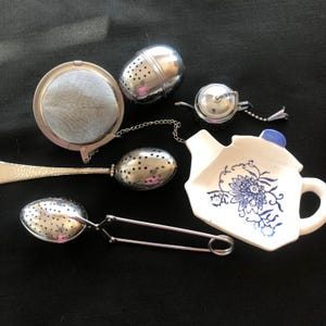 May include: Assortment of tea infusers and a ceramic tea bag holder. The infusers are made of stainless steel and include a ball, spoon, and basket style. The tea bag holder is white with a blue floral design.