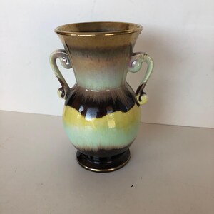 May include: A vintage ceramic vase with two handles. The vase features a color gradient of brown, yellow, and green. The rim and base have a gold trim. The vase is a decorative item.