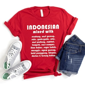 Könnte beinhalten: Ein rotes T-Shirt mit dem Text "INDONESIAN mixed with" und einer Liste indonesischer Gerichte. Das Shirt wird mit grauen Turnschuhen und Jeansshorts kombiniert. Der Text ist weiß.