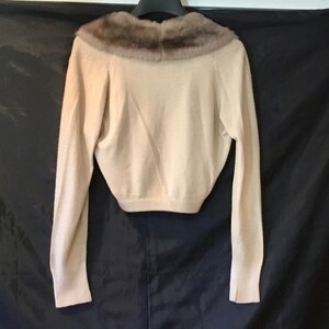 May include: A cream-colored knitted sweater with a brown fur collar. The sweater has long sleeves and a cropped length.
