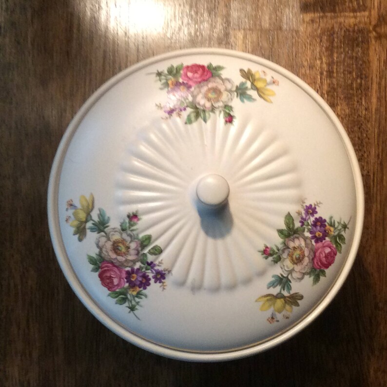 May include: White ceramic serving dish with a lid. The dish is decorated with a floral pattern in shades of pink, yellow, and green.