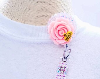 May include: A pink rose with a bee charm on a clear rhinestone badge reel.