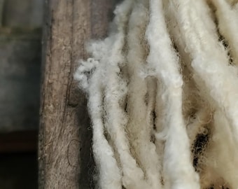 May include: Close-up of raw, off-white wool fibers cascading down a weathered wooden post. The wool appears soft and fluffy, with a slightly crimped texture. The natural fibers are likely for crafting or textile projects.