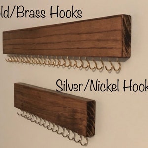 Puede incluir: Dos organizadores de joyas de pared de madera con ganchos. El organizador superior tiene ganchos dorados y el organizador inferior tiene ganchos plateados. El texto "Gold/Brass Hooks" est&aacute; sobre el organizador superior y el texto "Silver/Nickel Hooks" est&aacute; sobre el organizador inferior.