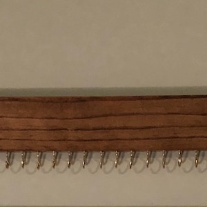 Puede incluir: Un organizador de joyas de madera con un tinte marr&oacute;n oscuro. Tiene 24 ganchos de metal para colgar aretes, collares o pulseras.